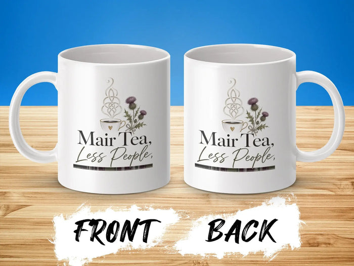 White mug with "Mair Tea, Less People" text and thistle design.