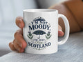White mug with "I'm not moody, I'm just from Scotland" and plaid umbrella design.