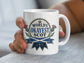 Mug with "World's Okayest Scot" text and Scottish thistle and flag.