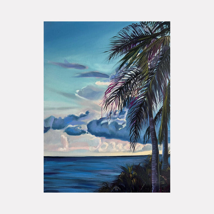 The artwork 'Solitude' by Claudia Robles-Gil captures a serene tropical seascape with a prominent palm tree framing the composition. Rich turquoise waters meet a dreamy sky filled with billowing clouds in shades of blue and pink. The palm fronds cast delicate shadows against the luminous sunset backdrop, creating a peaceful coastal atmosphere. Oil and acrylic on canvas, 24x18 inches.